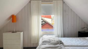 A bedroom with a sloped ceiling, a bed, a nightstand, a lamp, and a window with curtains.