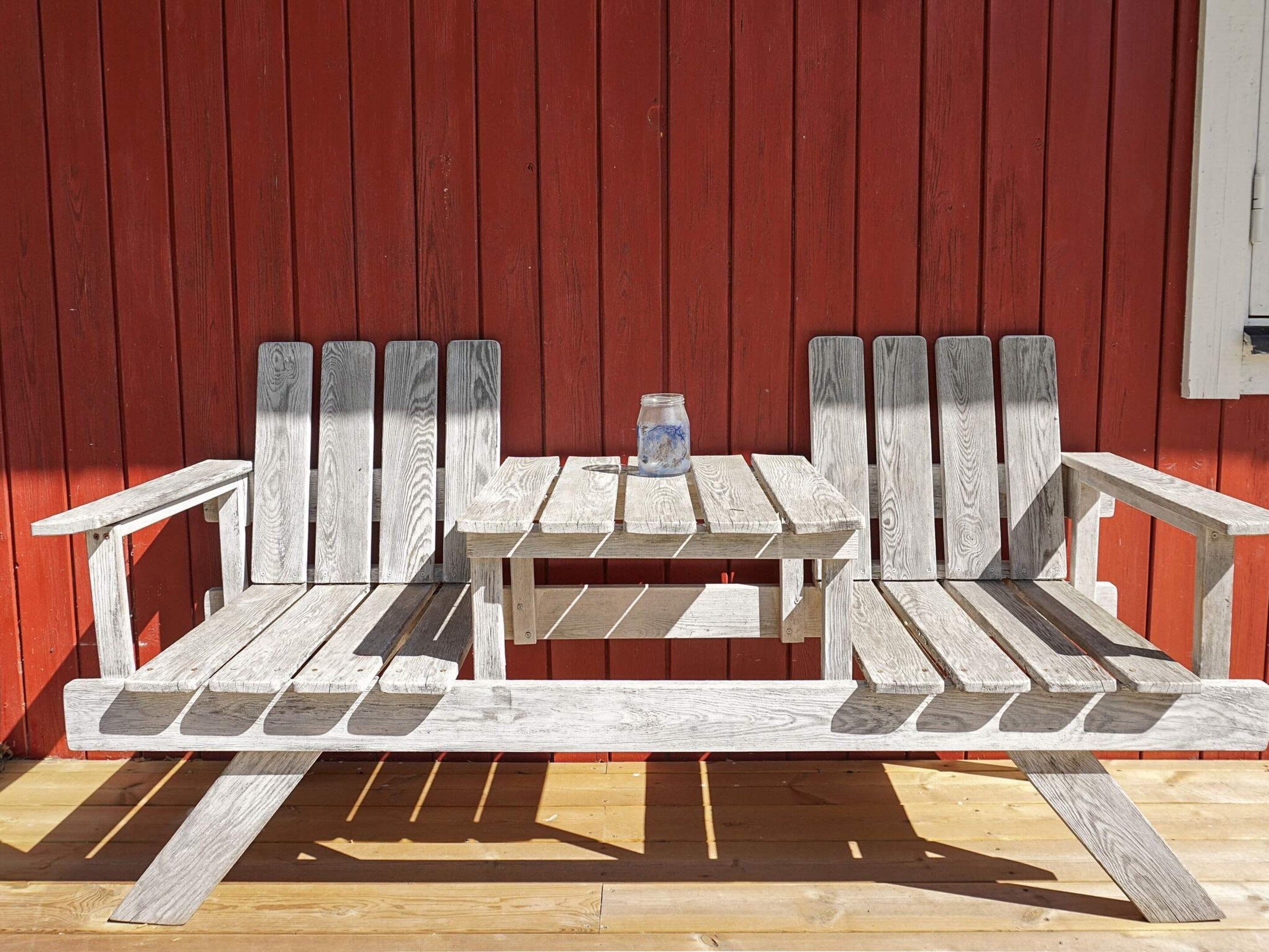 A wooden bench with a table in front of a red wooden wall.