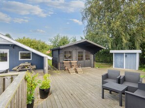 A wooden deck with outdoor furniture, a small shed, and a blue building with a window. - 4 Star Holiday Home in Sydals (Sydals)