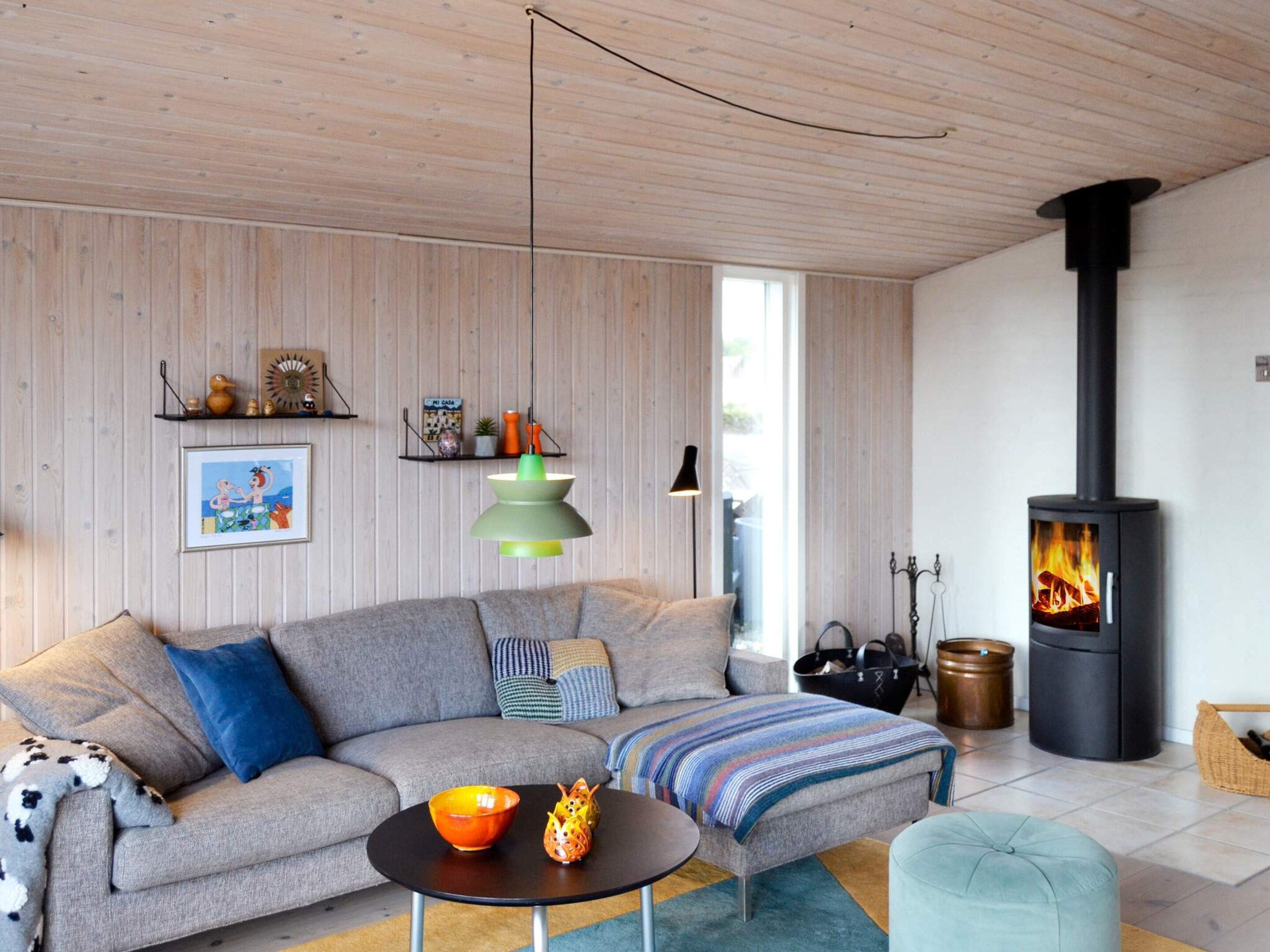 A modern living room with a sectional sofa, a round coffee table, a fireplace, and a wooden ceiling.