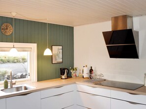 A kitchen with a sink, a clock, a hanging light, and a window with a view of greenery. - 6 Person Holiday Home in Fano (Fano)