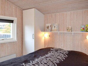 A bedroom with a bed, a window, a wardrobe, and wall-mounted shelves with decorative items.