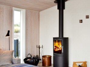 A modern interior with a wood-burning stove, a sofa, a window, and a lamp.
