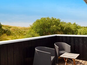 Een balkon met twee rieten stoelen en een bijzettafeltje, met uitzicht op een grasrijk landschap en bomen.