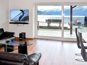 Een moderne woonkamer met een grote televisie, lederen meubels en uitzicht op een besneeuwde berg en een meer.