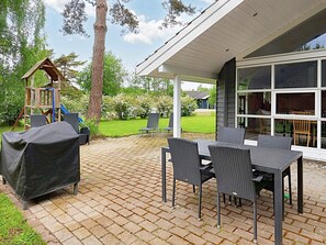An outdoor patio with a covered seating area, a play structure, and a view of the garden.