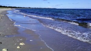 A beach with waves, a clear sky, and a distant shoreline. - 5 Star Holiday Home in Vaeggerlose (Vaeggerlose)