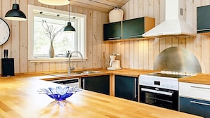 A modern kitchen with wooden walls, a large island, pendant lights, and built-in appliances. - 5 Star Holiday Home in Vaeggerlose (Vaeggerlose)