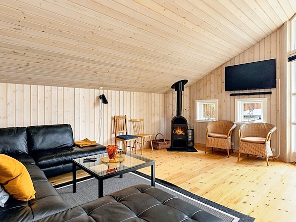 A cozy living room with a sofa, chairs, a coffee table, a fireplace, and a television mounted on the wall.