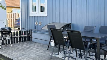 An outdoor patio with a table and chairs, a grill, and a blue building with a window.