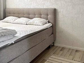 A bed with a grey upholstered headboard, white bedding, and a striped rug.