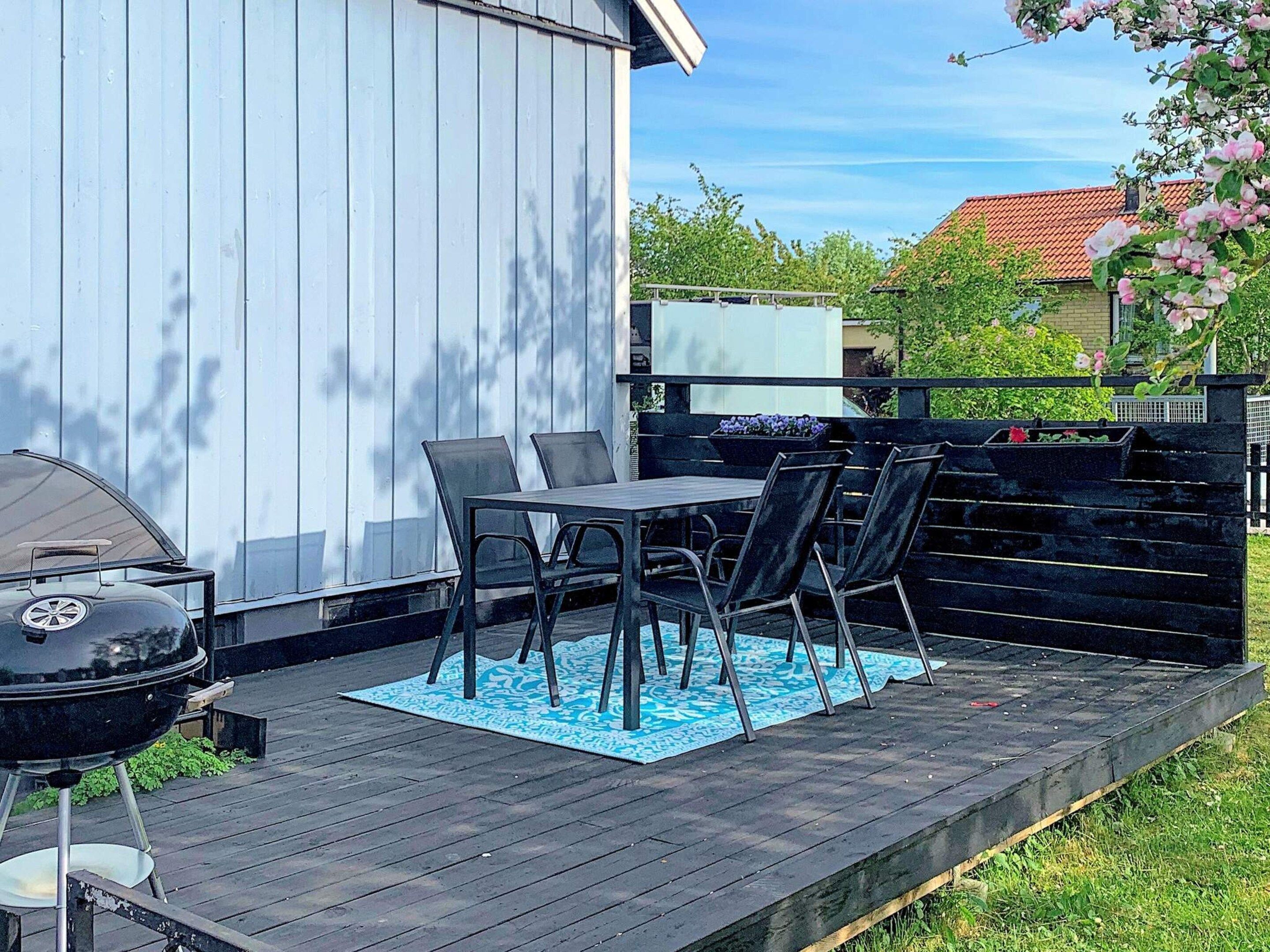An outdoor patio with a grill, a table with chairs, and a blue patterned rug.