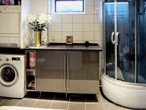 A compact bathroom with a washing machine, a cabinet with a small photo, and a glass shower enclosure.