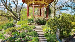 A gazebo with a red and yellow structure, surrounded by a garden with various plants and a stone staircase leading up to it. - 6 Person Holiday Home in Visby (Visby)