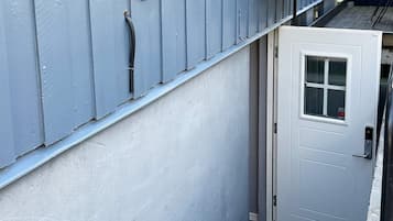 Une porte blanche avec une fenêtre, une rambarde en métal et un mur bleu percé de bouches d’aération.