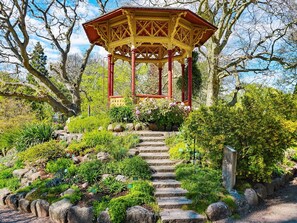A gazebo with a red and yellow structure, surrounded by a garden with various plants and a stone staircase leading up to it. - 6 Person Holiday Home in Visby (Visby)