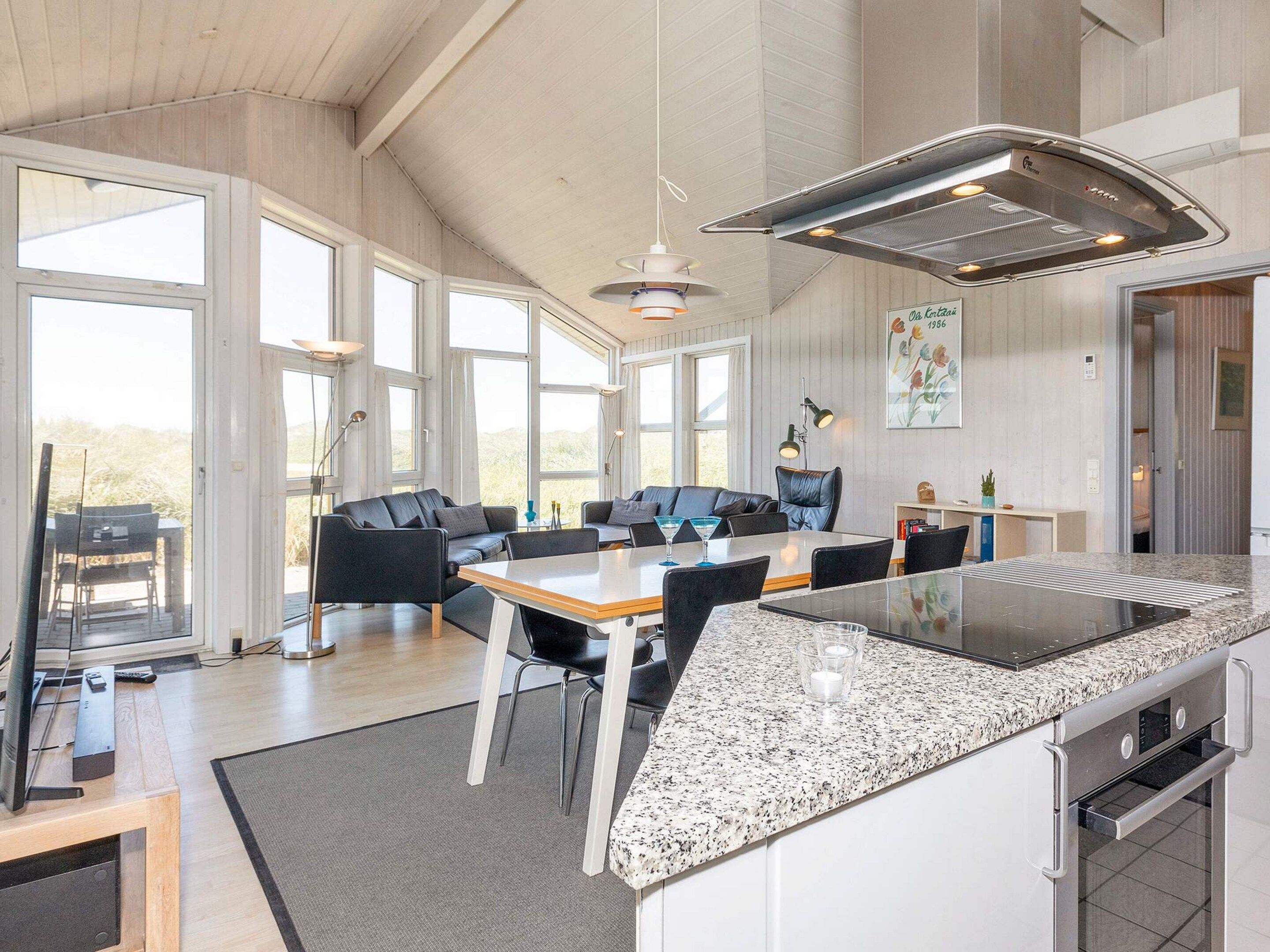 Una cocina moderna con una isla grande, comedor con sillas y vistas amplias a través de ventanas.