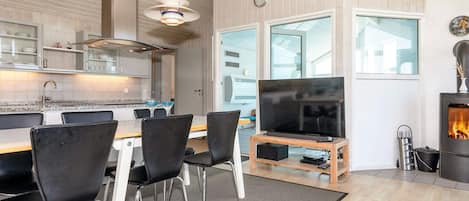A modern kitchen with a dining area, a flat-screen TV, and a wood-burning stove.