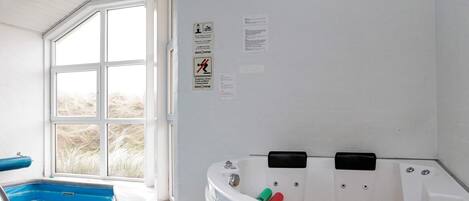 Un cuarto de spa con hidromasaje, una ventana con vista a la playa y una piscina.