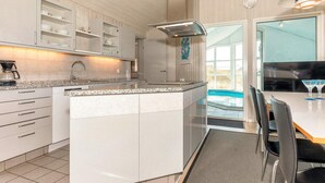 A modern kitchen with white cabinetry, a granite countertop, and a built-in island. There is a dining area with a table and chairs, and a view of a swimming pool through a glass door.