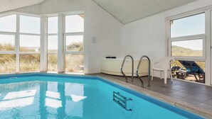 A swimming pool with clear blue water, large windows, and a view of the landscape.