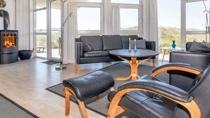 A modern living room with a fireplace, leather furniture, and large windows offering a view of the outdoors.