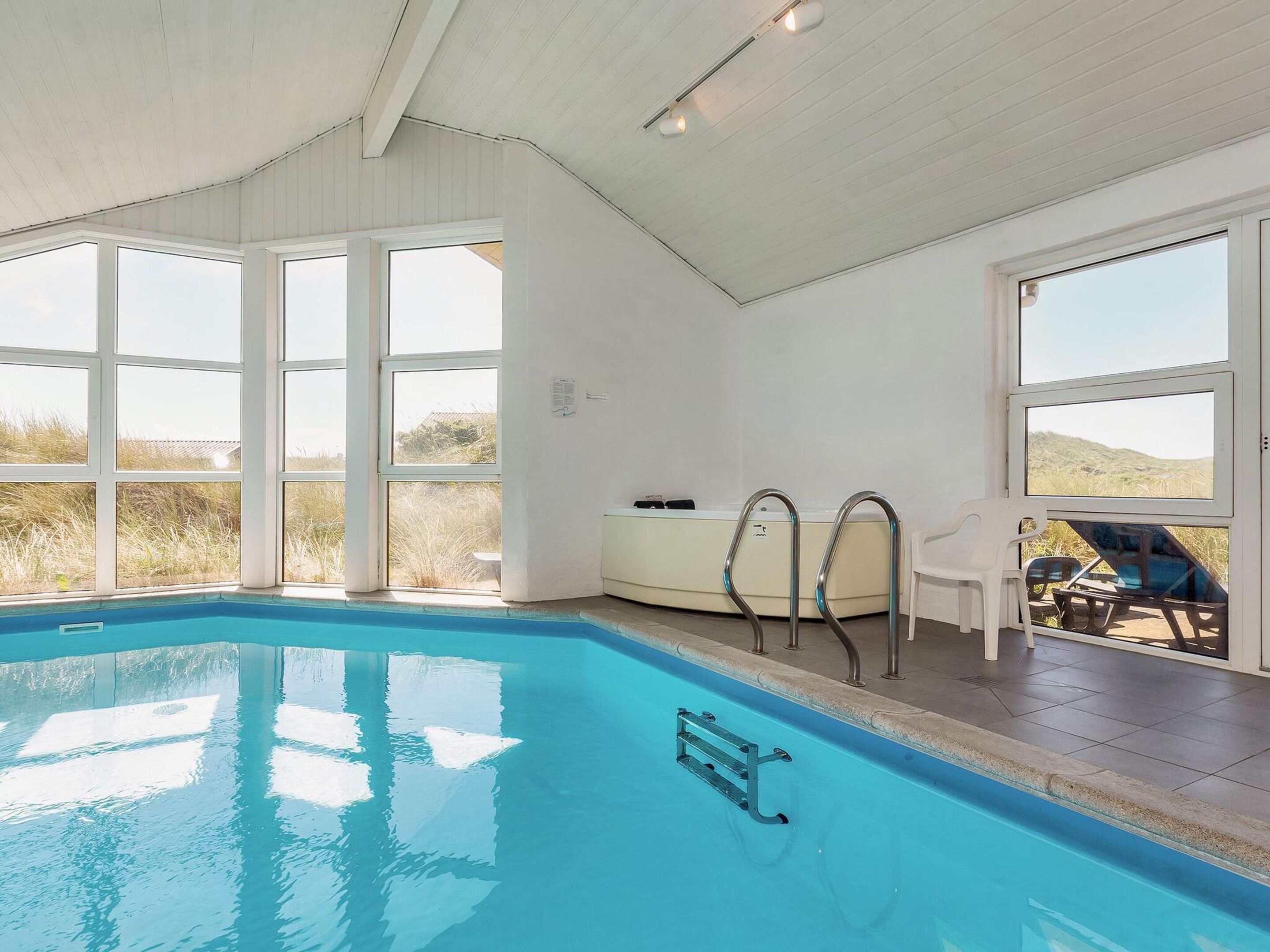 A swimming pool with clear blue water, surrounded by large windows offering views of the outdoors.