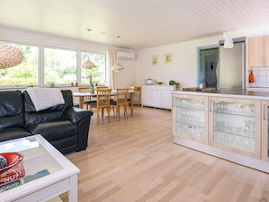 Eine moderne Küche mit weißen Schränken und einem Essbereich mit Holzkohle-Stühlen und einem schwarzen Sofa.