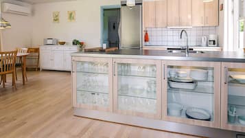 A modern kitchen with wooden cabinets, a central island with glass-fronted storage, a dining area with a wooden table and chairs, and a visible kitchen sink.