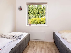 Ein Schlafzimmer mit zwei Betten, einem Fenster mit Blick auf Grünflächen, einem Heizkörper und einer Wandplatte.