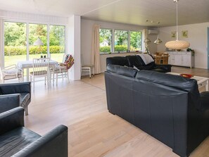 A modern living room with a large black sofa, a dining table with chairs, and a kitchen area in the background.
