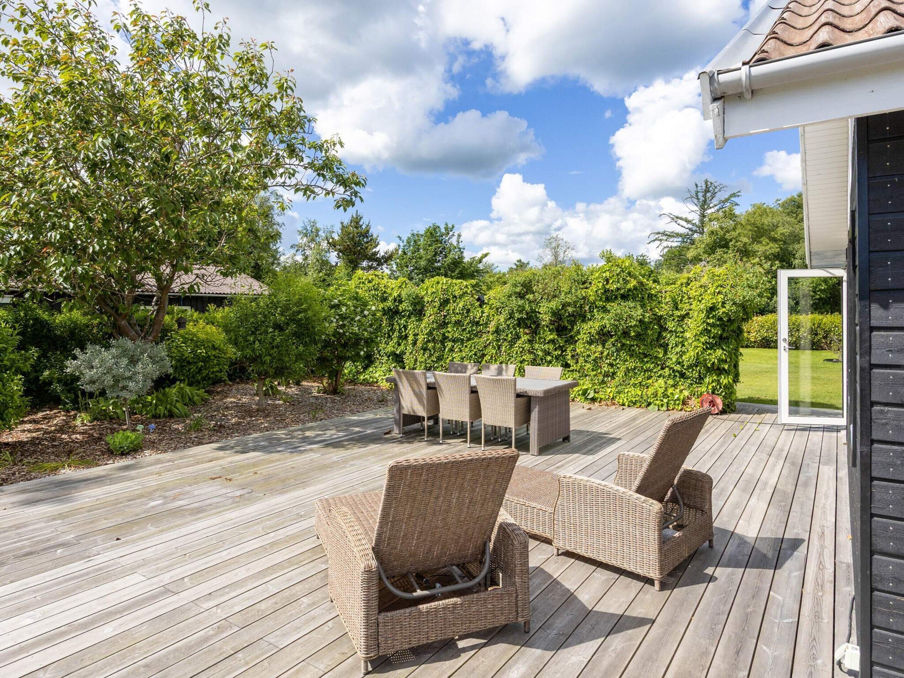 A wooden deck with wicker furniture and a glass door leading to a garden.