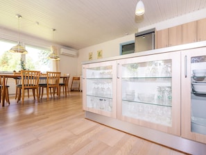 Eine moderne Küche mit Holzausstattung, Glastüren an den Regalen und einer Essecke mit Holzstühlen und Pendelleuchten.