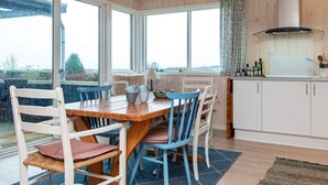 Eine gemütliche Küche mit Holztisch und -stühlen, großen Fenstern und Blick ins Freie.