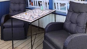 Ein überdachter Außenbereich mit zwei gepolsterten Stühlen und einem Tisch, dessen Tischplatte ein Mosaik aufweist.