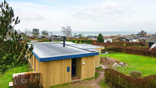 Ein modernes Holzgebäude mit flachem Dach, gelegen in einer Wohngegend mit Häusern und Blick auf das Meer.