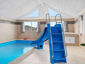 An indoor swimming pool with a blue slide, a ladder, and a view of the outside.