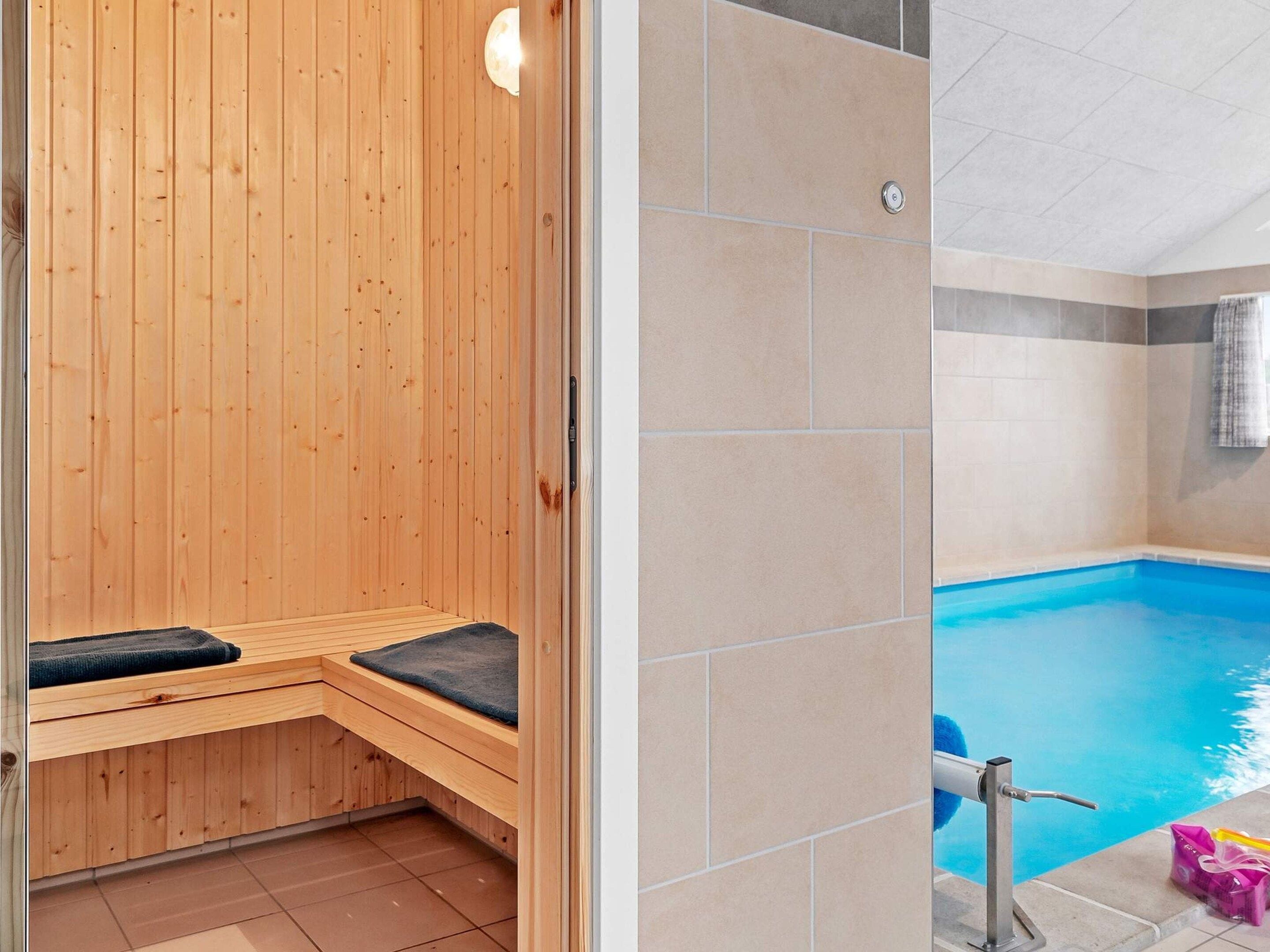 A wooden sauna with a bench and a pool area with a pool ladder.