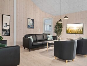 A modern living room with a black leather sofa, a coffee table, and a TV mounted on the wall.