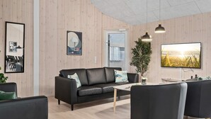 A modern living room with a black leather sofa, a coffee table, and a TV mounted on the wall. - Holiday Home in Kappeln (Kappeln)