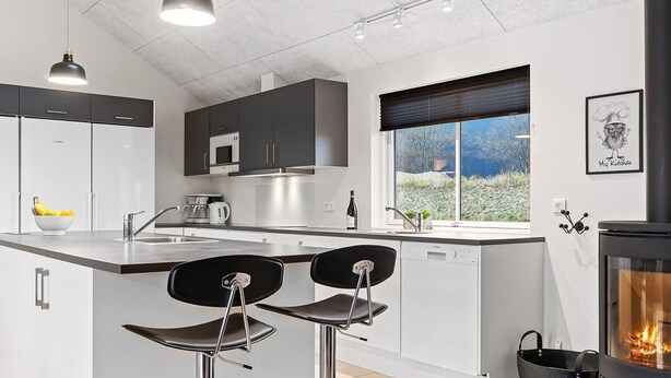 A modern kitchen with a central island, bar stools, a stove, and a window with a view. - Holiday Home in Kappeln (Kappeln)