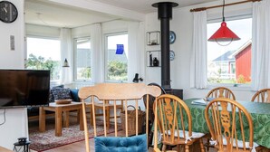 Een gezellige woonkamer met een houten eettafel, stoelen, een blauwe fauteuil, een televisie en een zwart fornuis.