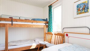 Een slaapkamer met stapelbed, een raam, een stoel en een schilderij aan de muur.