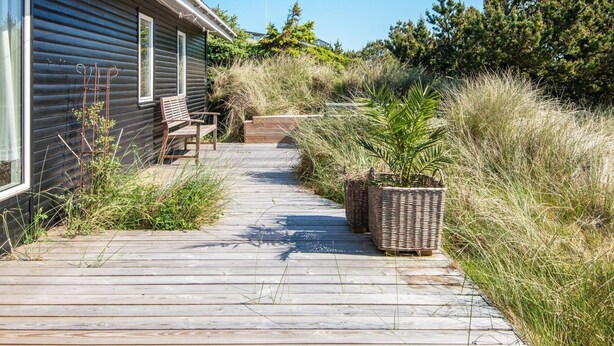 Een houten terras leidt naar een huis met een bank en rieten manden.