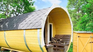 Une structure cylindrique jaune, dotée d’une porte, d’une rampe et d’un petit espace de porche aménagé avec des rondins de bois et un banc.