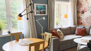 Un salon chaleureux avec une table ronde en bois, un canapé gris agrémenté de coussins, un lampadaire et un tableau accroché au mur.