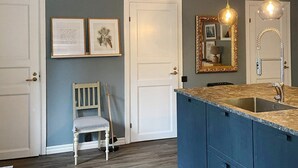 Une cuisine avec un îlot central bleu, des portes blanches et des œuvres d’art encadrées accrochées au mur.