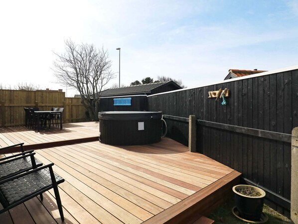 Una terraza de madera con un jacuzzi, una mesa con sillas y una valla de madera.