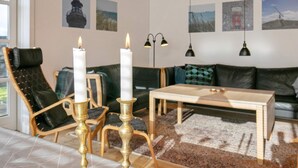 A modern living room with a sofa, two chairs, a coffee table, and two lit candles on brass candlesticks. - 7 Person Holiday Home in Skagen (Skagen)