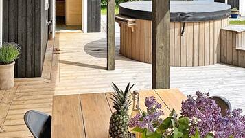 Una terraza de madera con un jacuzzi, una mesa con una piña y flores, y sillas.